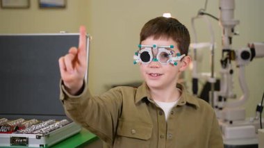Deneme çerçevesi takan çocuk göz hareketi ve odaklanma yeteneğini gösteren göz muayenesi sırasında farklı yönlere işaret ediyor.