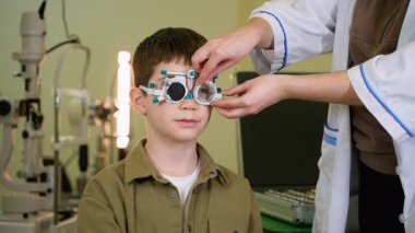 Modern tıp kliniğinde kesin görsel keskinlik değerlendirmesi için uzman bir deneme çerçevesi kullanarak genç hastaya kapsamlı göz muayenesi yapan profesyonel bir göz doktoru.