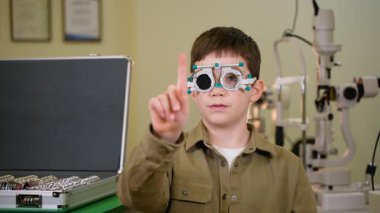 Göz doktorunun talimatı doğrultusunda çeşitli yönleri gösteren, göz muayenesi sırasında deneme çerçevesi takan çocuk hasta.