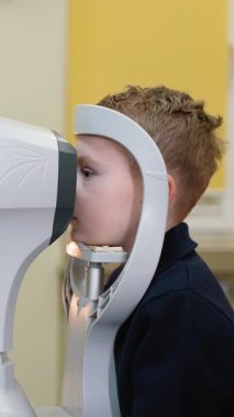 Pediatrik oftalmolojist, çocuk hastaları tam otomatik tarama yapıyor, doğru gözlük reçetesi saptaması için dikkatli bir şekilde ölçüm hatası yapıyor.