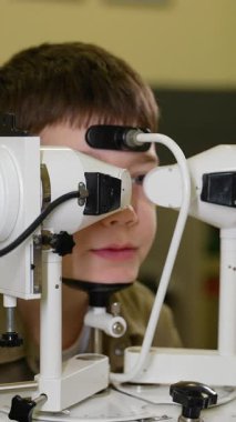 Oftalmoloji kliniği doktoru özel ekipman kullanan çocuk hastaların görme yetilerini inceliyor, görsel keskinliği kontrol ediyor ve doğru tedavi için potansiyel göz sorunlarını teşhis ediyor.