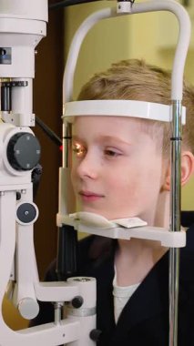 Gelişmiş tıbbi ekipmanlar kullanılarak sabırla göz muayenesine tabi tutulan genç çocuk vizyonu için düzenli kontrollerin önemini gösteren