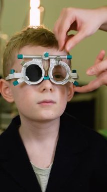 Profesyonel optometrist, pediatrik göz bakımı muayenesi sırasında genç hastaların görme yetilerini kesin görsel keskinlik değerlendirmesi için deneme çerçevesini kullanarak dikkatlice inceliyor.