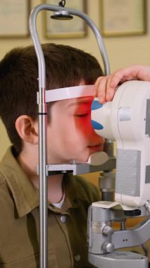 Modern tıp kliniğinde kapsamlı pediatrik göz muayenesi sırasında ileri seviye otomatik fraktör kullanan genç bir hastanın hassas görme taraması yapan profesyonel bir optometrist.