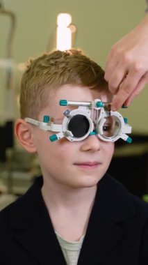 Yetenekli bir optometrist, genç hastaları dikkatlice inceliyor. Görme ve tanısal değerlendirmeler için test çerçevesi lenslerini düzenli olarak ayarlıyor.