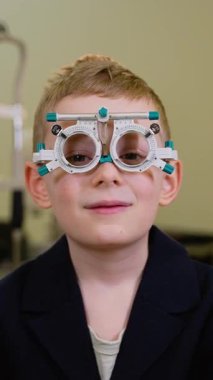 Göz muayenesi sırasında göz çerçevesi takan mutlu çocuk, bu deneyimden duyduğu memnuniyeti dile getirerek onay işareti yapıyor.