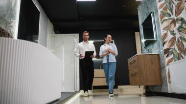 Profesyonel danışman, kadına banyo mobilyaları seçimi, tasarım tercihlerini keşfetme ve lüks, modern sergi salonu ortamında detaylar satın alma konusunda rehberlik ediyor.