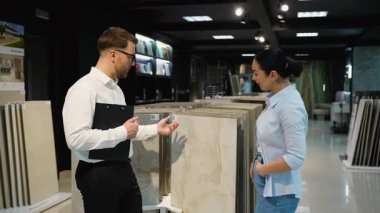 Profesyonel danışman modern bir galeride bir kadına çeşitli fayans seçeneklerini sunuyor. Proje için dokuları, renkleri ve uygunluğu tartışıyor.