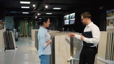 Profesyonel danışman, modern bir sergi salonundaki fayansları seçen bir kadına ev yenileme projesi için rehberlik ve uzmanlık sağlıyor.