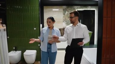 Profesyonel danışman, kadın müşteriye farklı banyo mobilyası seçeneklerini gösteriyor, stil, malzeme ve yenileme projesinin planlarını tartışıyor.