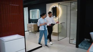 Profesyonel banyo tasarım danışmanı sunar lavabo, fayans ve fikstür seçenekleri sunar ve modern sergi salonu iç mimarisi danışmanlığı sırasında bayan müşterilere rehberlik eder.