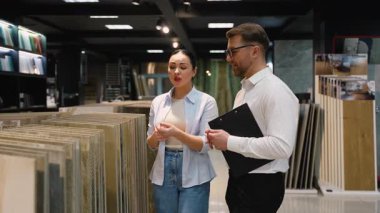 Modern bir galeride bir danışman ile fayans seçeneklerini tartışan kadın müşteri, yenileme projesi için çeşitli materyaller ve tasarımlar keşfediyor.