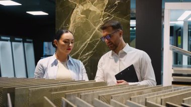 Modern bir sergi salonundaki müşteriye çeşitli fayans örnekleri gösteren profesyonel danışman, seçenekleri tartışıyor ve ev yenileme veya iç tasarım projesi için uzman tavsiyeleri sunuyor