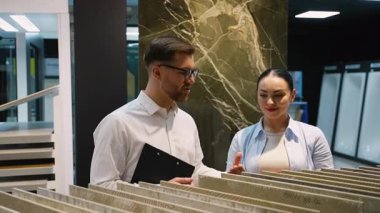 Profesyonel tasarım danışmanı, kadın müşteriye fayans seçimi sürecinde rehberlik ederek gösterişli, modern sergi salonu ortamında uzman tavsiyesi veriyor.