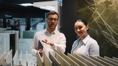 Modern sergi salonunda kadın müşteriye fayans seçimi sürecinde rehberlik eden profesyonel iç mimari danışmanı, ev yenileme projesi için malzeme seçeneklerini araştırıyor