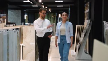 Nalburdaki fayansları seçen, farklı örnekleri tartışan ve işaret eden, apartman yenileme için satın alma kararı veren profesyonel danışman.