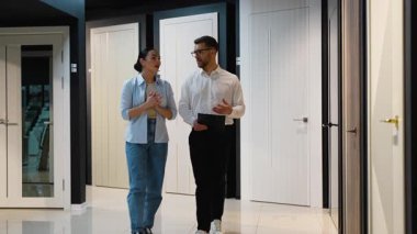 Mobilya mağazasında kadın müşterilere çeşitli modern iç kapılar gösteren profesyonel erkek danışman, farklı seçeneklerin avantajlarını ve dezavantajlarını anlatıyor