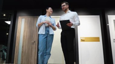 Kadın müşteriye çeşitli kapı modelleri gösteren satıcı, özellikleri tartışıyor ve ev yenileme projesi için doğru seçimi yapmasına yardım ediyor.