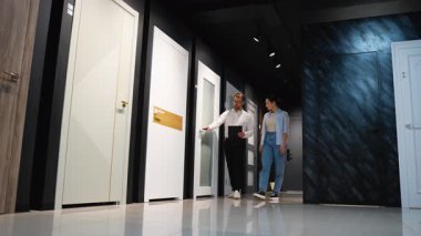 Potansiyel müşterilere iç kapılar sunan profesyonel bir satıcı, modern sergi salonundaki seçim sürecini detaylı ürün danışmanlığı ile yönetiyor.