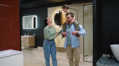 Gülümseyen ebeveynler ve oğulları bir galeride banyo demirbaşlarını seçerken iyi vakit geçiriyorlar. Baba, oğlunu omuzlarında taşıyor.
