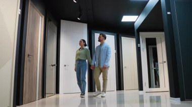 Genç çift, iç kapılar seçilirken profesyonel rehberlik alıyor. Çağdaş sergi salonunda birbirlerine yakın duruyorlar. Ev yenileme için tasarım seçeneklerini tartışıyorlar.