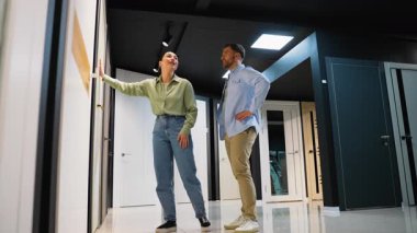 Profesyonel danışman bir çifte kapı ve fayans seçiminde yardımcı oluyor, çeşitli seçenekler sunuyor ve modern bir sergi salonunda tercihleri tartışıyorlar.