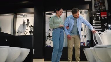 Aile klozet almak için tesisat dükkanına gidiyor. Profesyonel kadın danışman. Ev yenileme işlemi sırasında erkek müşterilere çeşitli modeller sunuyor.