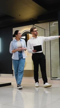 Profesyonel danışman kadın müşteriye çeşitli banyo armatürlerini gösteriyor, seçenekleri tartışıyor ve modern sergi ortamında rehberlik ediyor.