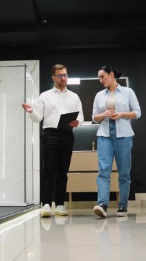 Modern sergi salonundaki yenileme seçeneklerini tartışırken fayans, tesisat ve kapı seçimlerinde müşteriye rehberlik eden profesyonel tuvalet danışmanı.