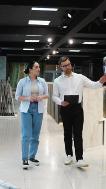 Profesyonel danışman kadın modern bir sergi salonundaki bir çifte farklı fayans seçenekleri gösteriyor. Ev yenileme projeleri için malzeme ve tasarımları tartışıyorlar.