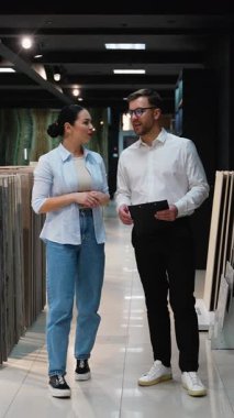 Modern sergi salonunda fayans seçen müşterilere yardımcı olan profesyonel danışman, uzman tavsiyesi sunuyor ve ev yenileme projesi seçeneklerini tartışıyor