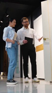 Modern bir galeride müşteriye çeşitli kapı modelleri sunan profesyonel iç mimar, ev yenileme projesi için özellikler ve tasarım seçeneklerini tartışıyor