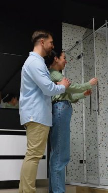 Sevgi dolu bir çift, banyo mobilya dükkanında bir duş kabini seçiyor, özelliklerini inceliyor ve tercihlerini satış asistanıyla tartışıyor.