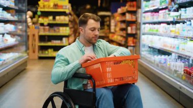 Engelli bir adam kendi başına alışveriş yapar, markette gezinirken, neşeli ifadeli raflardan yiyecek seçer, kişisel özerkliğini gösterir.