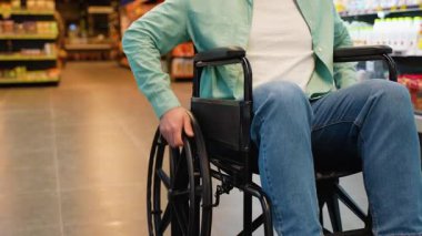 Bağımsız tekerlekli sandalye kullanıcısı süpermarket koridorlarında güvenle dolaşır, bakkaliyeleri bağımsız seçer ve perakende ortamda kusursuz hareketlilik gösterir