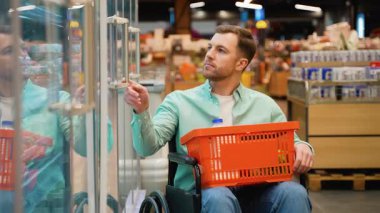 Tekerlekli sandalye kullanıcısı marketin soğutulmuş bölümünden dikkatlice bir kutu yumurta seçer. Bu da günlük alışverişe bağımsızlık ve dahil olma durumunu gösterir.