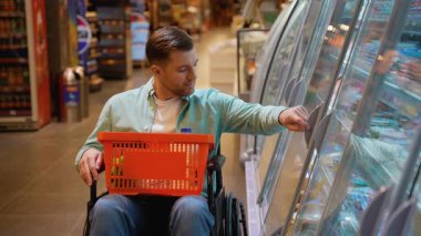 Bağımsız alışveriş yapan, dondurulmuş gıda ürünlerini dikkatle incelerken dondurulmuş gıda ürünlerini dikkatle inceleyen, odaklanmış kararlılıkla bakkaliye seçen genç bir adam.