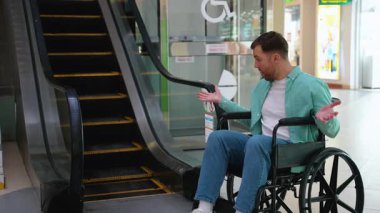 Tekerlekli sandalye kullanıcısı bir yürüyen merdivenin eteğindeki hayal kırıklığını belirterek, kamu alanlarını mimari engellerle dolaşmada engelli insanların karşılaştığı zorlukları vurguluyor.
