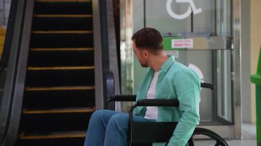 Kendine güvenen tekerlekli sandalye kullanıcısı başını modern asansörün yakınına çevirip, kentsel alışveriş ortamında ulaşılabilirlik ve kişisel bağımsızlığı temsil ediyor.