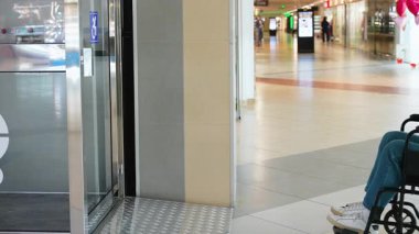 Tekerlekli sandalyedeki kullanıcı, yoğun alışveriş merkezinin içindeki asansörde, engelliler için bağımsız hareketlilik ve bariyersiz erişimi vurguluyor