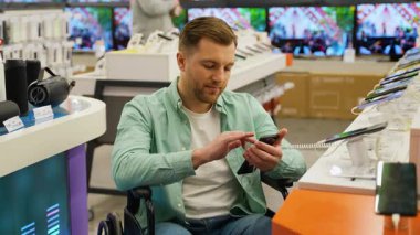 Tekerlekli sandalye kullanıcısı modern elektronik mağazasında akıllı telefon özelliklerini dikkatlice inceleyerek erişilebilir alışveriş ve bağımsız teknoloji keşiflerini vurguluyor