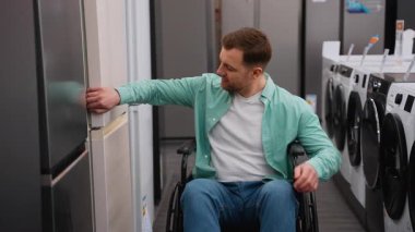 Engelli bir adam buzdolabı raflarını karıştırıyor, özellikleri değerlendiriyor ve ev aletleri mağazasında kişisel özerklik ile gezinirken satın alma kararı alıyor