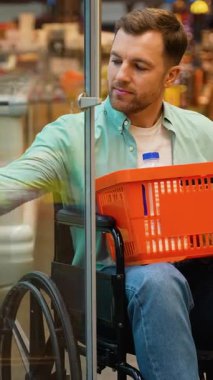 Tekerlekli sandalyeye bağlı süpermarket soğutmalı bölümde gezinen, yumurtaları bağımsız olarak seçen ve kendine güvenen bir gülümsemeyle alışveriş sepetinin içine yerleştiren