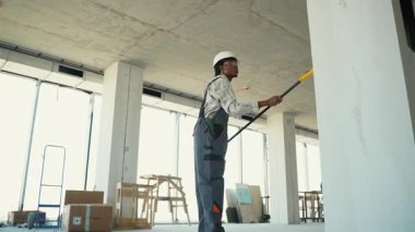 Profesyonel müteahhit lazer metreyle yeni inşaat alanının içindeki mesafeyi ölçüyor, güvenlik kaskı takıyor ve hassas mimari proje geliştirme için gelişmiş teknolojiyi kullanıyor.