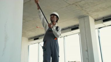 Güvenlik gözlüğü takan profesyonel bir ressam. İnşaat halindeki yeni bir binanın duvarlarını ve tavanlarını boyamak için teleskopik boya silindiri kullanıyor.