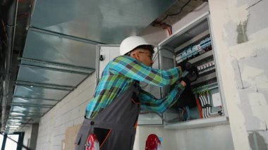 Yetenekli elektrikçi hassas elektrik paneli bakımı yapıyor, kabloları bağlıyor ve sigorta kutusuna profesyonel güvenlik ekipmanlarıyla otomatik anahtarlar yerleştiriyor.