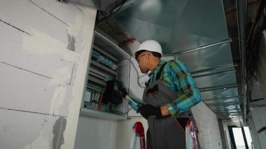 Profesyonel elektrikçi, elektrik paneli içine kablo bağlamak ve bileşenleri yerleştirmek, inşaat halindeki bir binaya güvenlik ve işlevsellik sağlamak için titizlikle çalışıyor.