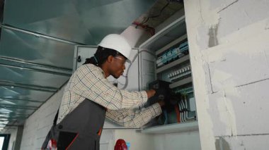 Profesyonel elektrikçi, elektrik panelini güvenlik teçhizatıyla yüklüyor. Aktif inşaat alanında teknik uzmanlık örneği gösteriyor.