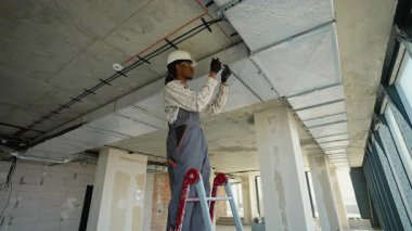 Profesyonel elektrikçi, inşaat halindeki bir binaya kablo tepsisi ve kablo döşeme sistemi kurarak güvenlik ve verimliliği sağlamak için dikkatli çalışır.