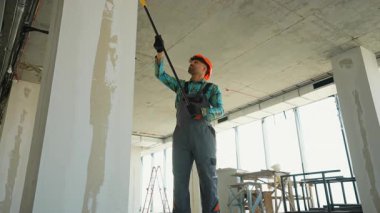 Profesyonel ressam uzun bir silindirle astar kullanarak yüzeyi yapım aşamasındaki bir binanın son resmine hazırlar.